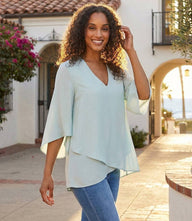 Woman wearing a silky crepe Bracelet Sleeve Asymmetric Top with a V-neck, flare sleeves, and layered asymmetrical hem