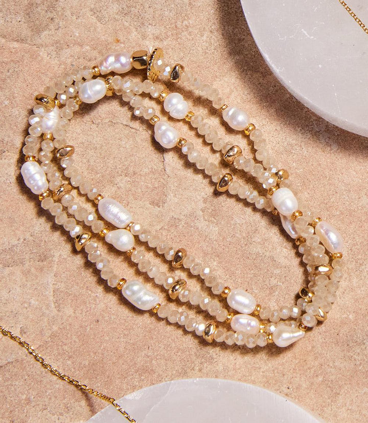Champagne-toned beaded gemstone and pearl stretch bracelet with crystal and metal beads displayed on a textured surface