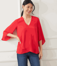 Petite size bracelet sleeve asymmetric red top in silky crepe with layered hem and flare sleeves worn by smiling woman