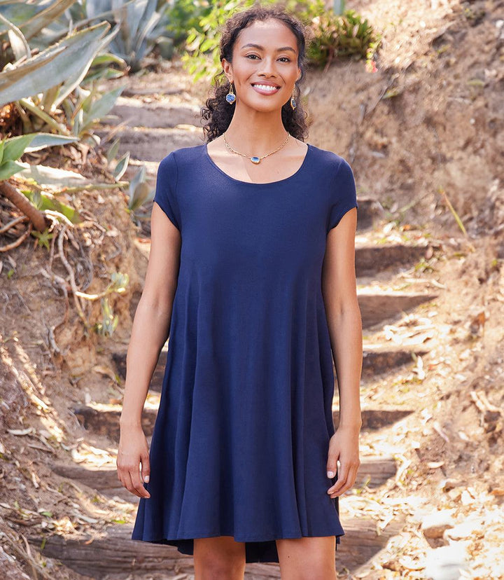 Woman wearing a navy blue Maggie Trapeze Dress with cap sleeves, boat neckline, and high-low hem standing outdoors on stone steps