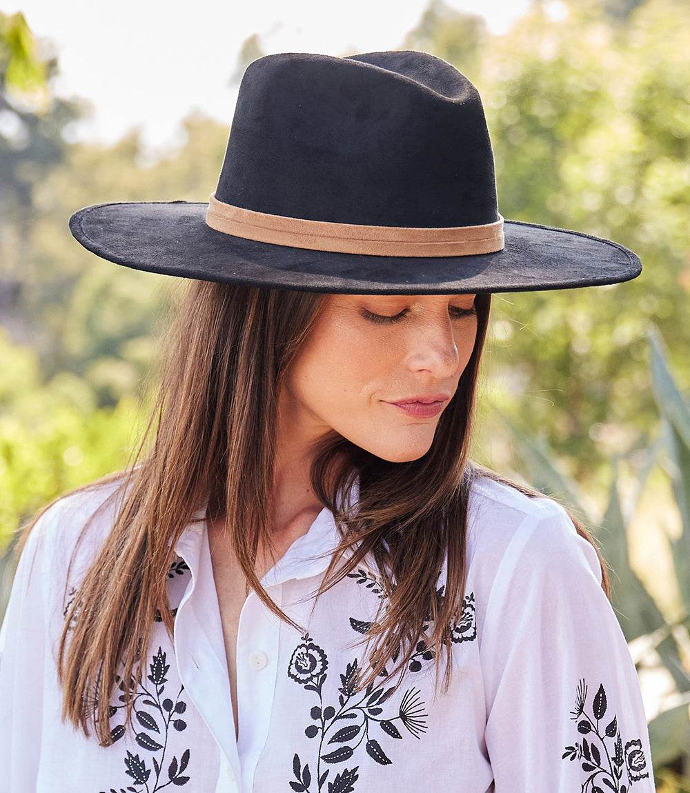 Woman wearing black faux suede fedora hat with tan band outdoors
