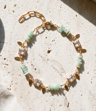 Crystal and gemstone bracelet with aqua gemstones, crystal accents, gold paperclip chain, and lobster clasp on white background