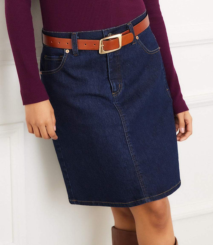 Woman wearing dark blue denim short skirt with belt loops and brown belt, paired with a long-sleeve purple top.
