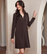 Woman wearing a black zip-up travel dress with long sleeves and a collar, standing indoors near an archway