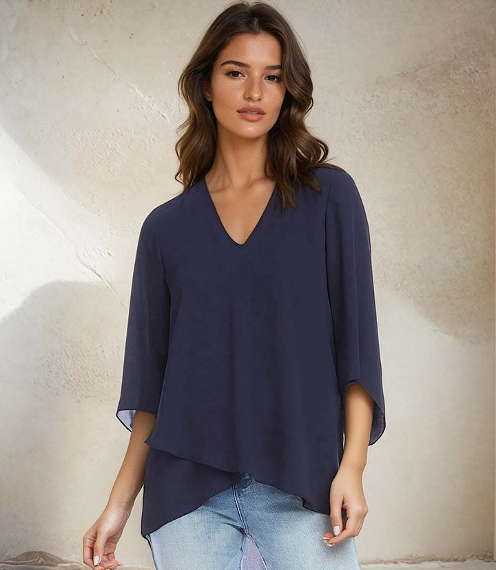Woman wearing navy blue silky crepe Bracelet Sleeve Asymmetric Top with V-neck, flare sleeves, and layered asymmetrical hem.