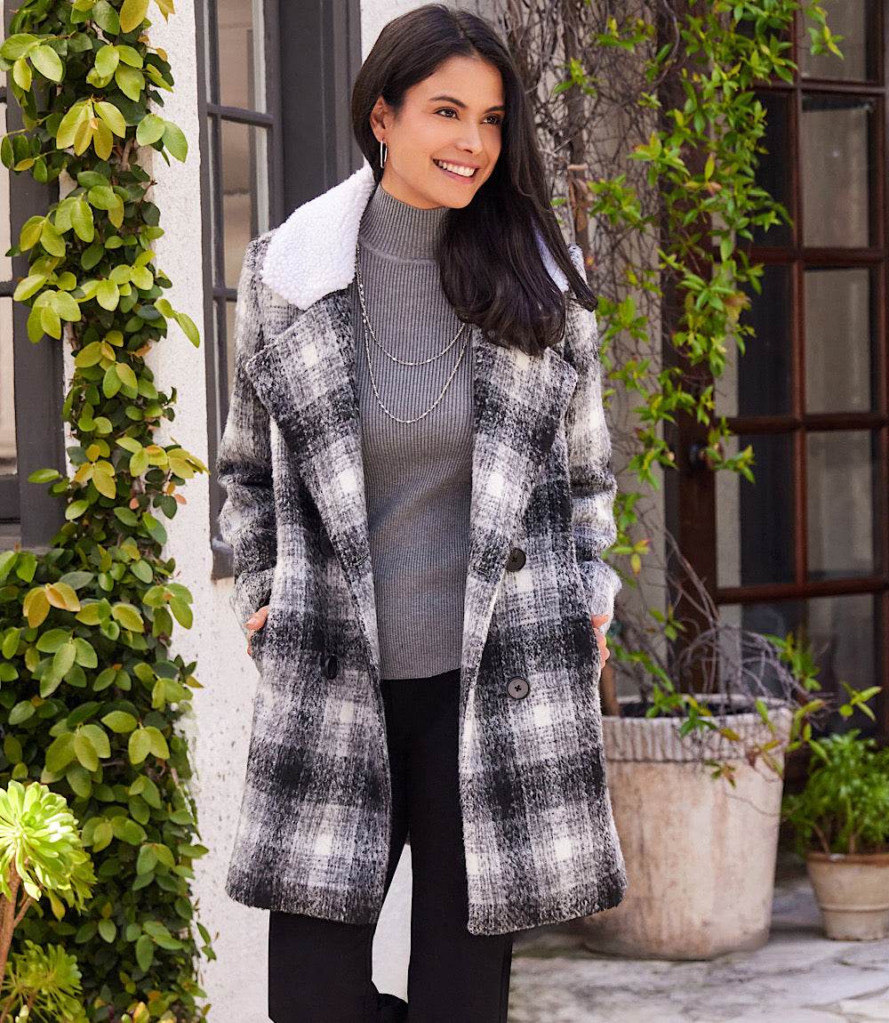 Woman wearing a black and white plaid shearling collar coat with black tortoiseshell buttons outdoors