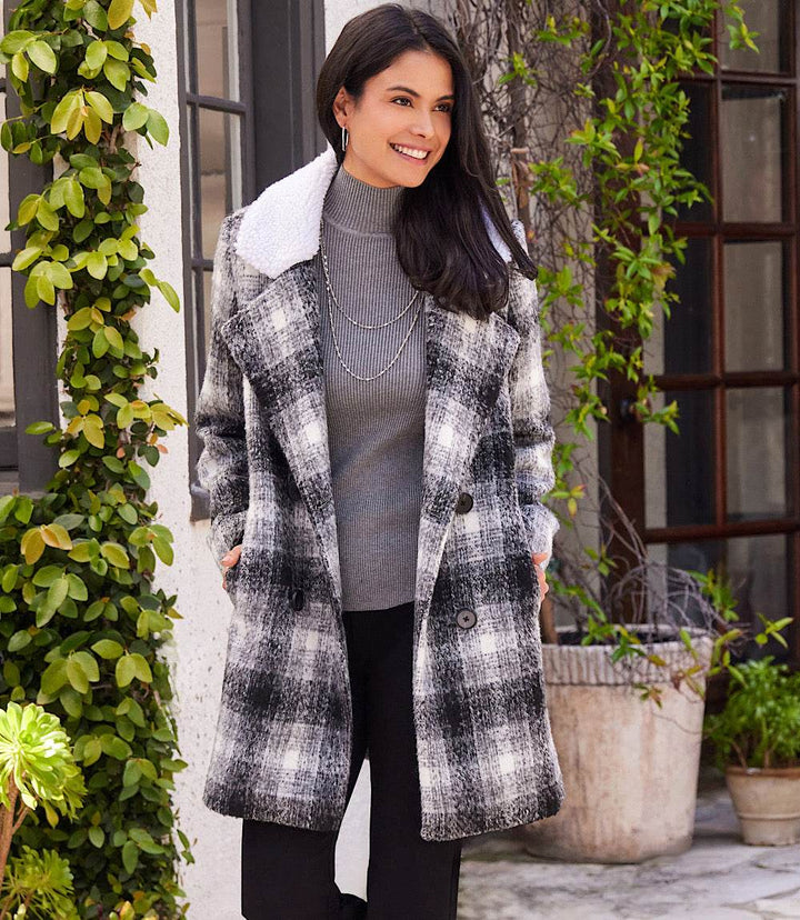 Woman wearing a black and white plaid shearling collar coat with black tortoiseshell buttons outdoors