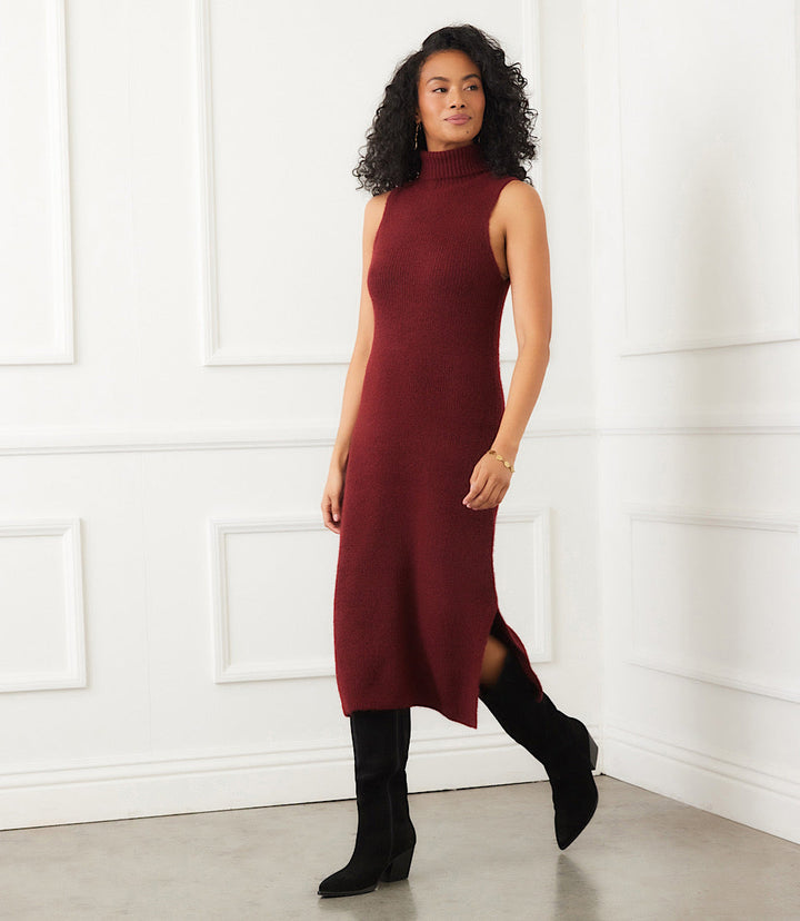 Woman wearing sleeveless turtleneck sweater dress in burgundy with side slit and ribbed edges