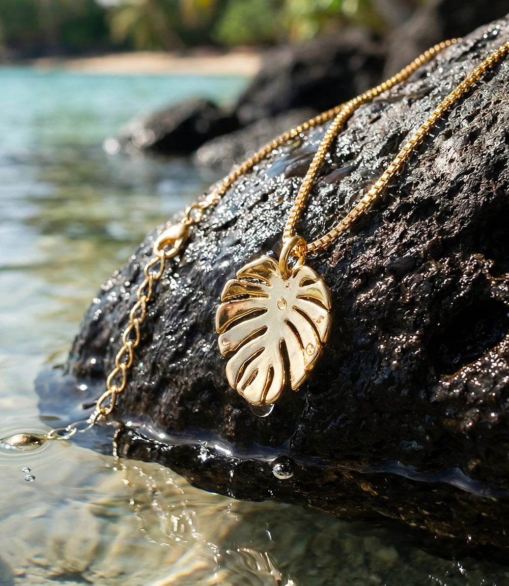 Close-up of tropical leaf charm necklace with polished gold-tone leaf pendant on 18K gold plated chain