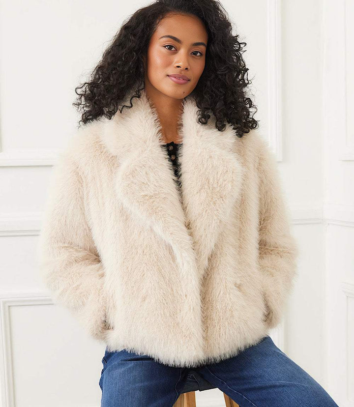 Woman wearing a cream-colored cropped faux fur jacket with wide notched collar and button front closure.