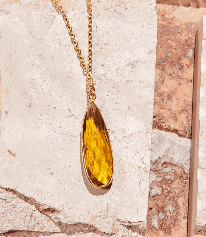 Citrine quartz pendant necklace with gold chain on stone background