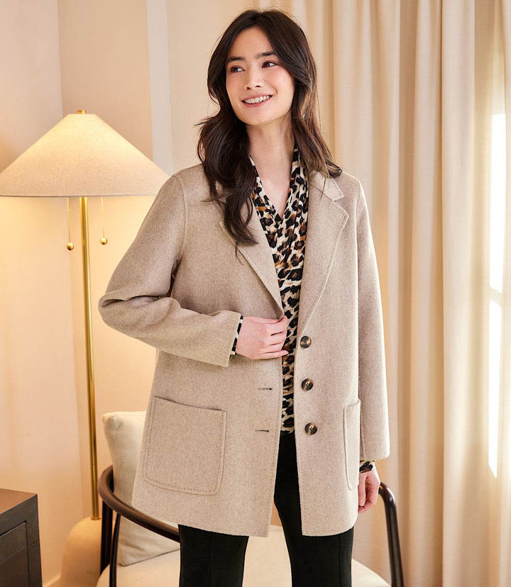 Woman wearing oversized brushed blazer in beige with three buttons and front patch pockets indoors
