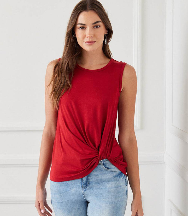 Woman wearing a red sleeveless pick-up top with a crew neck and twist hem paired with blue jeans