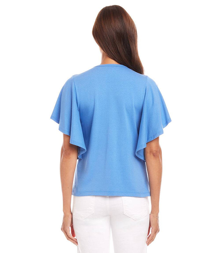Back view of a woman wearing a blue flutter sleeve V-neck top with flouncy sleeves and white pants