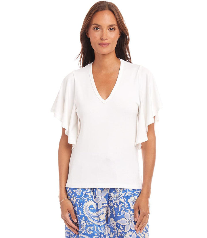 Woman wearing white flutter sleeve top with v-neck and ruffled sleeves paired with blue patterned pants