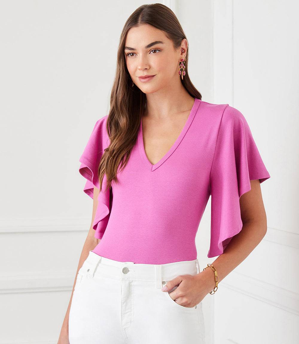 Woman wearing a pink flutter sleeve top with v-neck and ruffled sleeves paired with white pants