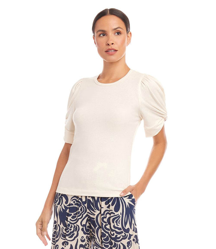 Woman wearing beige twist sleeve top with puff sleeves and crew neck, paired with patterned pants