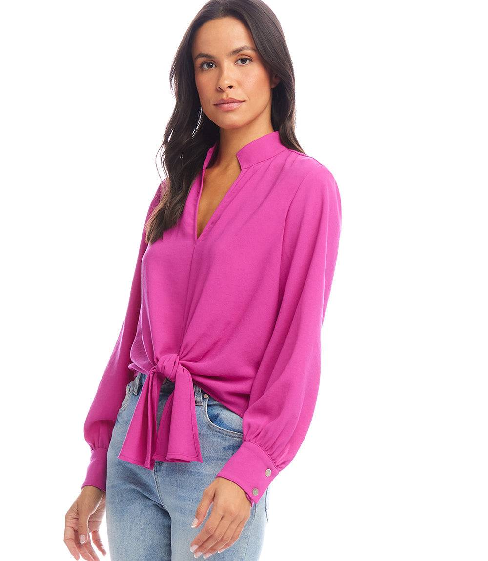Woman wearing a vibrant pink long sleeve tie-front top with a mandarin collar and light blue jeans.