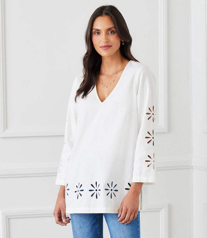 Woman wearing white cutout embroidered flower detail tunic with V-neck and long sleeves paired with blue jeans