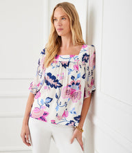 Woman wearing floral contrast square neck top with ruffled puff sleeves and shirring detail, paired with white pants