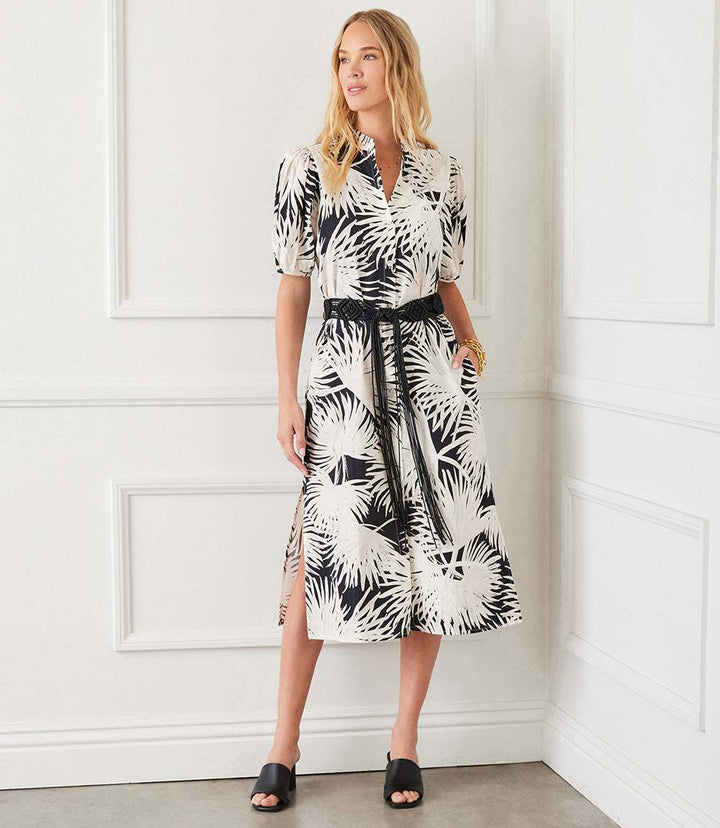 Woman wearing a puff sleeve midi shirtdress with black palm print, braided belt, side pockets, and side slit.