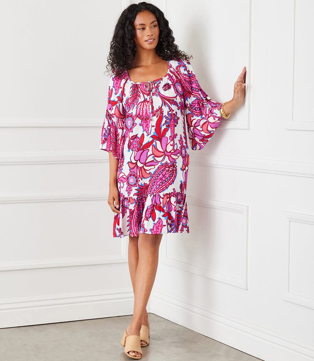 Woman wearing a peony paisley print ruffle hem dress with bell sleeves and tassel neck ties.