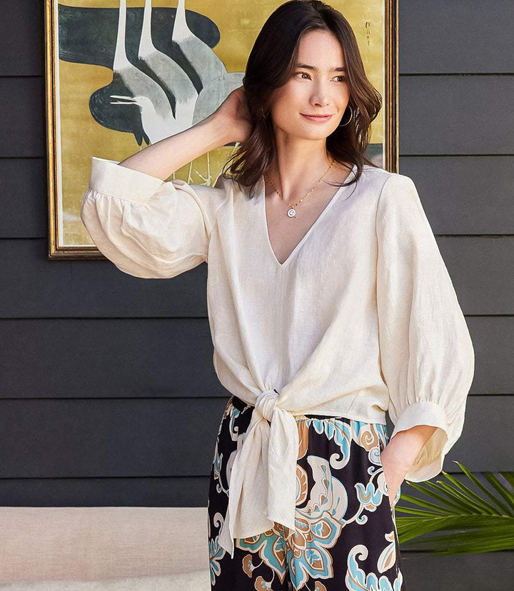 Woman wearing a beige blouson sleeve linen top with a front tie hem and V-neck.