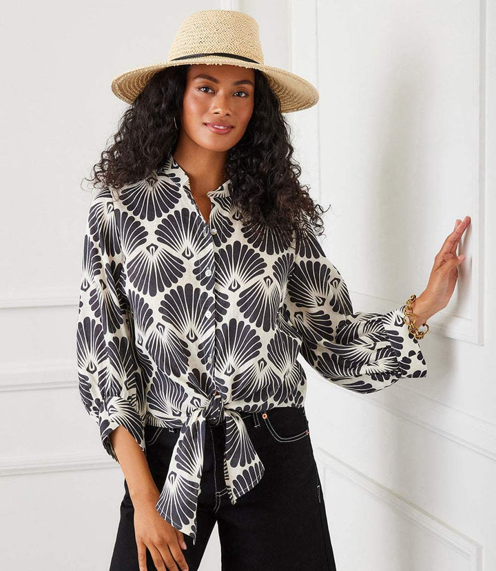 Woman wearing a black and cream sea shell print blouson sleeve linen tie-front top with 3/4 bishop sleeves and mandarin collar.
