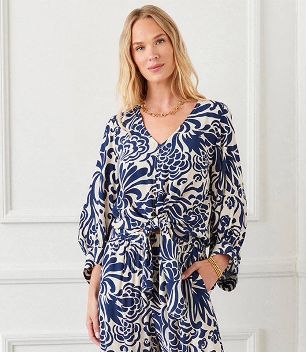 Woman wearing a cream blouson sleeve tie front top with whimsical blue paisley print and V-neck.
