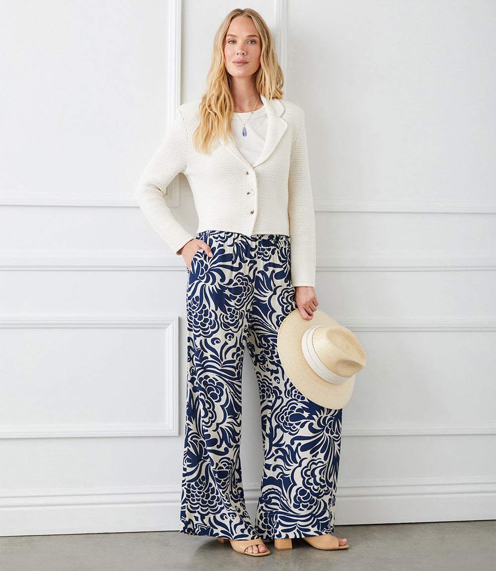 Woman wearing navy and cream wide leg pants with whimsical paisley print paired with white jacket holding a straw hat