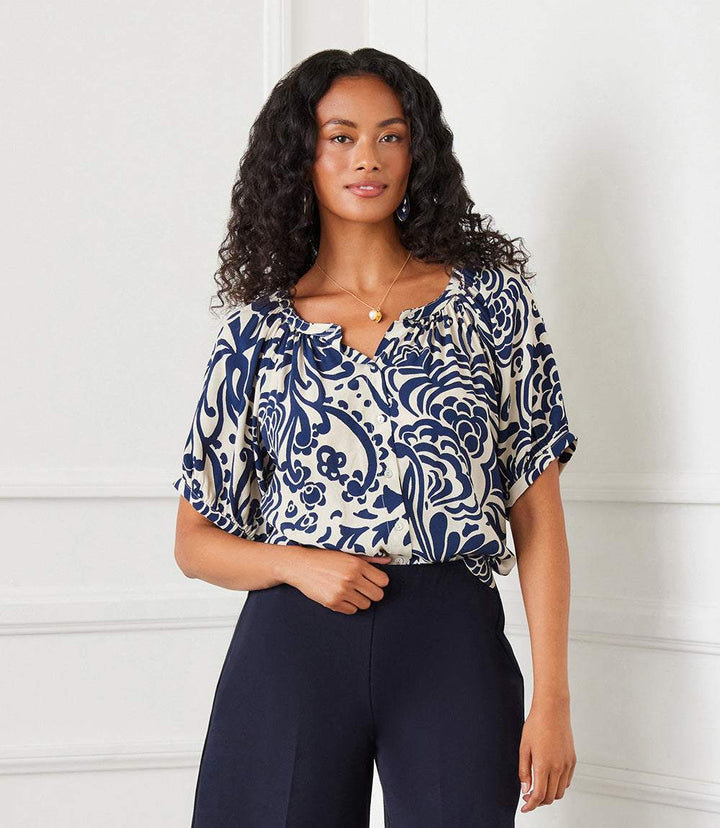 Woman wearing a short sleeve peasant top with navy paisley print and puff sleeves paired with dark pants