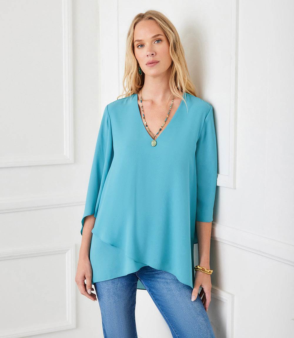 Woman wearing a teal Bracelet Sleeve Asymmetric Top with V-neck and layered asymmetrical hem paired with blue jeans.