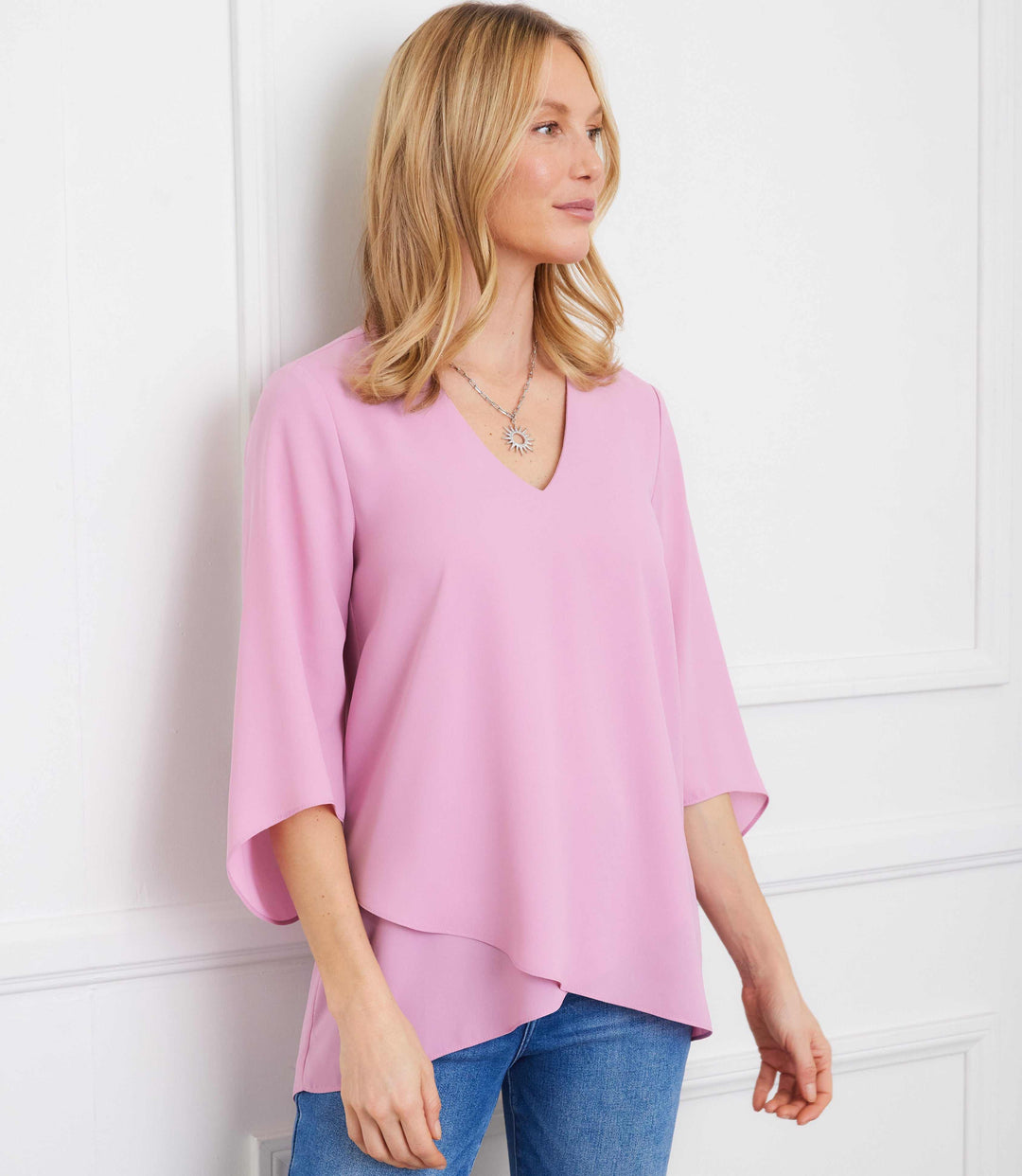 Woman wearing a pink silky crepe bracelet sleeve asymmetric top with V-neck and layered hem paired with blue jeans