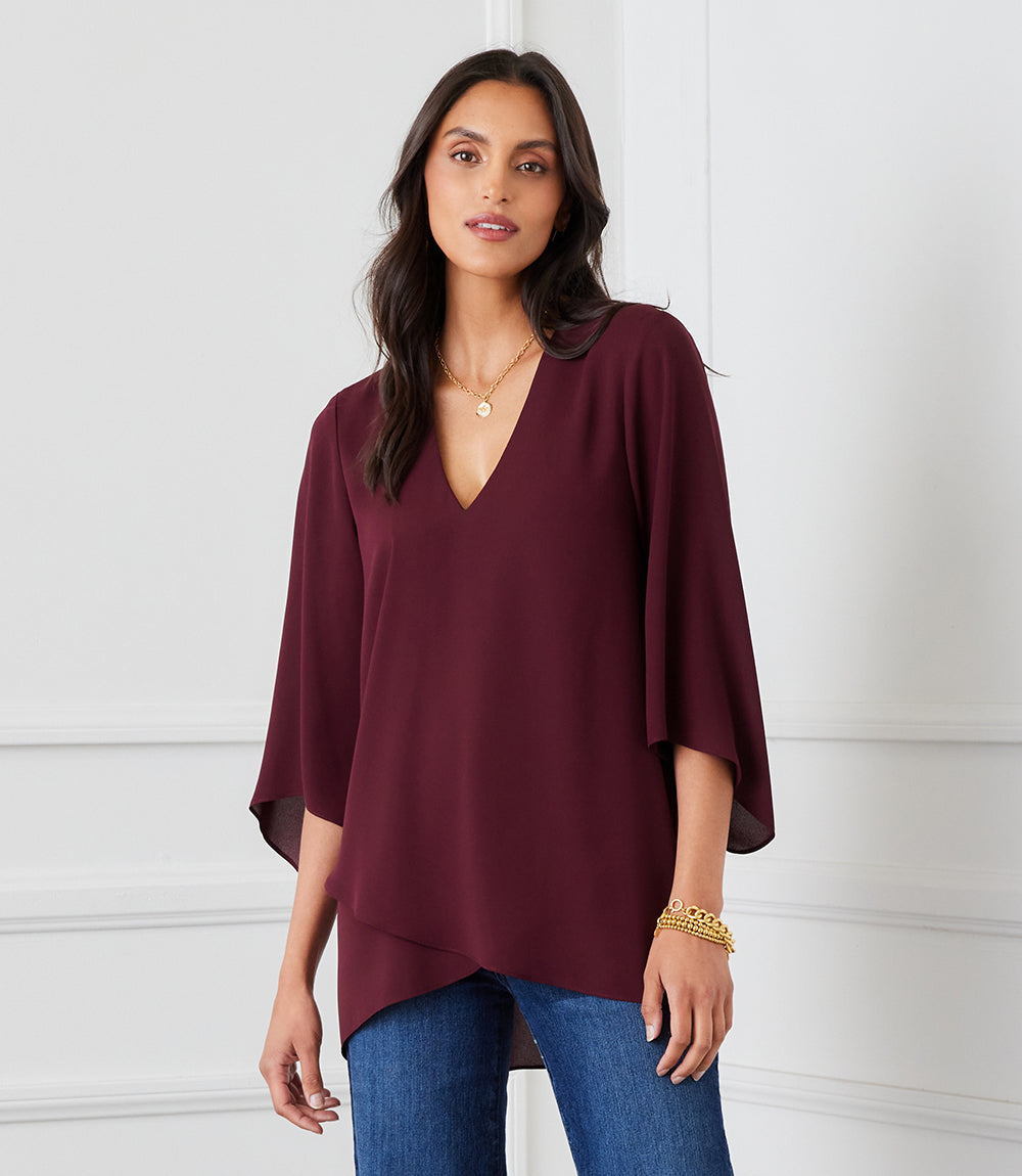 Woman wearing a burgundy bracelet sleeve asymmetric top with V-neck and layered hem