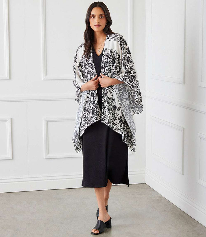Woman wearing black dress with black and white open front jacket with floral scarf print and asymmetrical hem