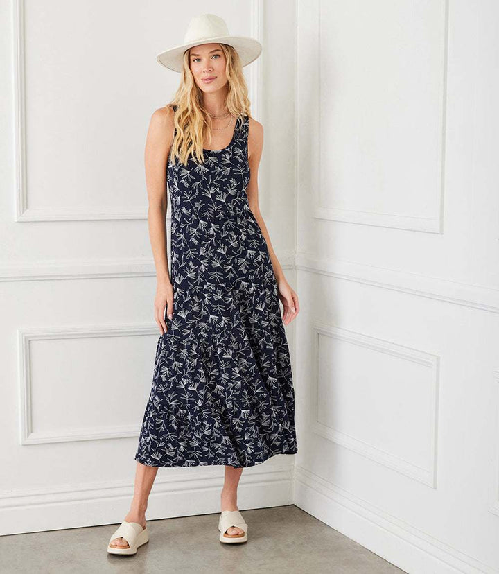 Woman wearing sleeveless tiered midi dress with white floral print on navy background and a white hat indoors
