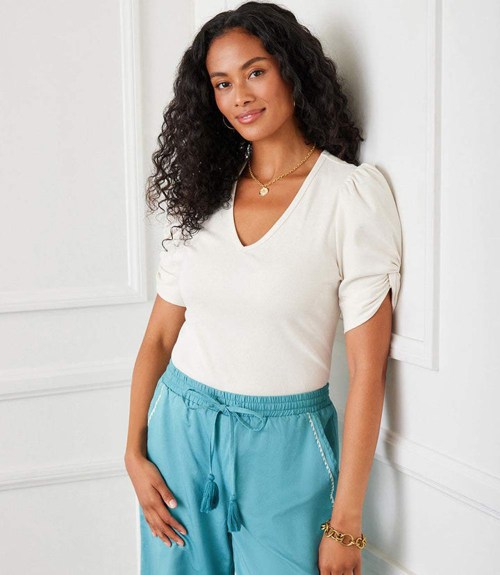 Woman wearing a white ribbed twist sleeve V-neck top with puff sleeves and blue drawstring pants
