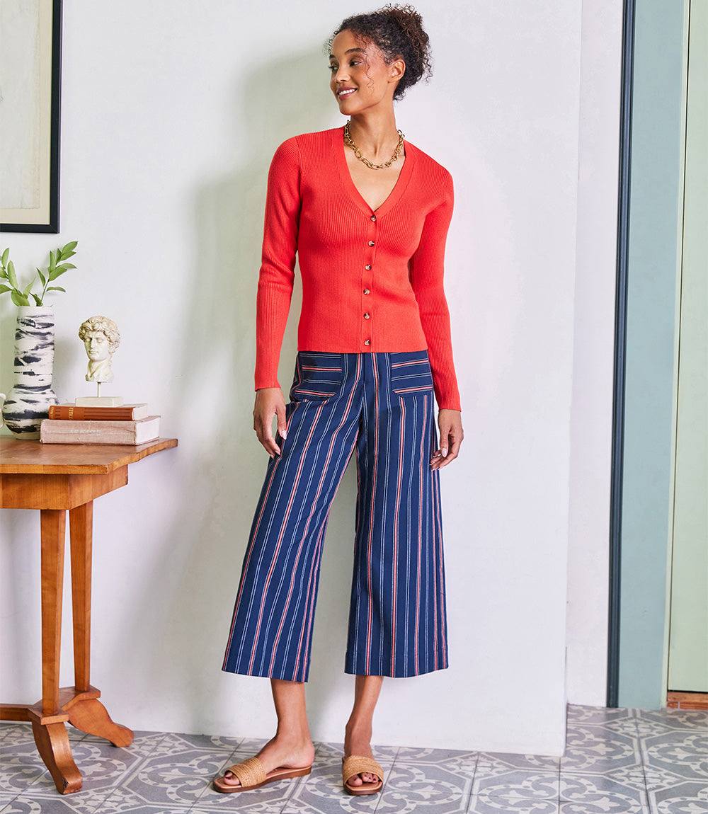 Woman wearing navy stripe cropped wide leg pants with orange accents and a red button-up top in a modern indoor setting