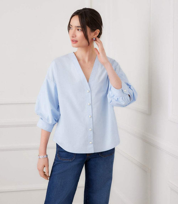 Woman wearing white lantern sleeve pearl button top with V-neck and gathered cuffs