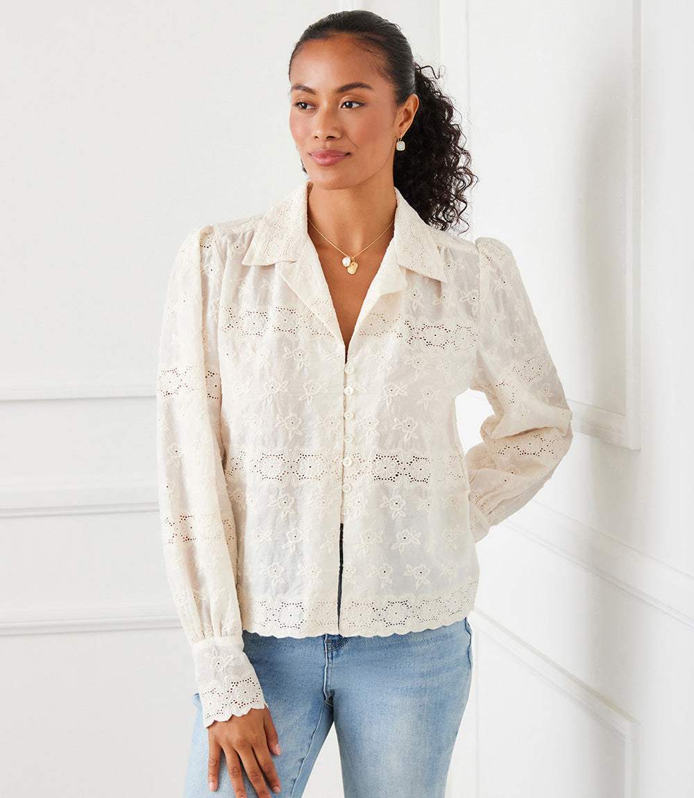 Woman wearing a long sleeve embroidered blouse with scalloped hem and cuffs, featuring floral eyelet details and a relaxed fit.