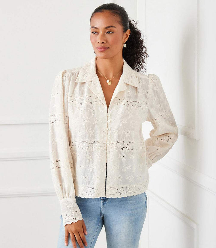 Woman wearing a long sleeve embroidered blouse with scalloped hem and cuffs, featuring floral eyelet details and a relaxed fit.