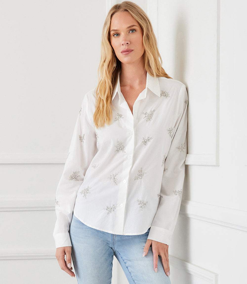 Woman wearing white embellished button up shirt with beaded details and shell buttons