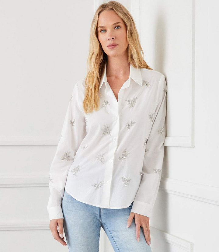 Woman wearing white embellished button up shirt with beaded details and shell buttons