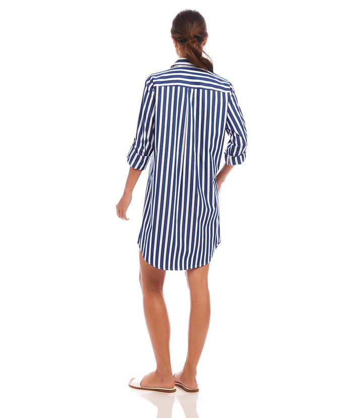 Back view of a woman wearing a navy and white vertical striped roll tab stripe shirtdress with rolled-up sleeves and shirttail hem.