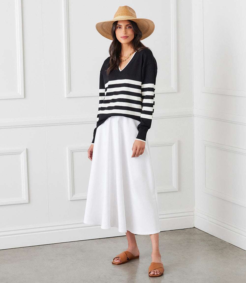 Woman wearing black and white stripe V-neck sweater with oversized fit and ribbed edges paired with white skirt and tan hat