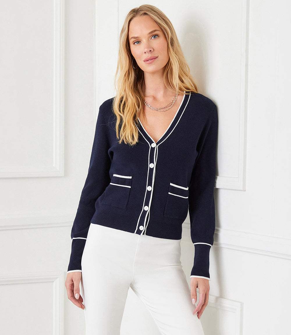 Woman wearing navy contrast trim cardigan sweater with white buttons and pockets paired with white pants