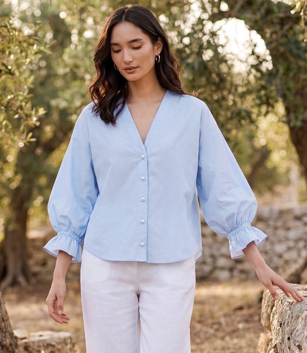 Woman wearing white cotton poplin lantern sleeve top with pearl buttons and V-neck