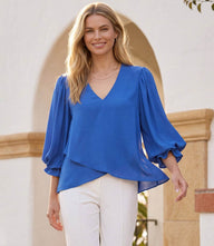 Woman wearing a layered sleeve asymmetric top with V-neck and gathered shoulders in silky crepe fabric