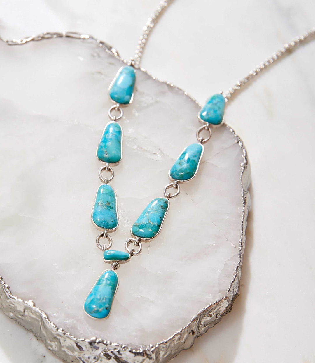 Sterling silver necklace with linked turquoise stones and vertical pendant design on white marble background