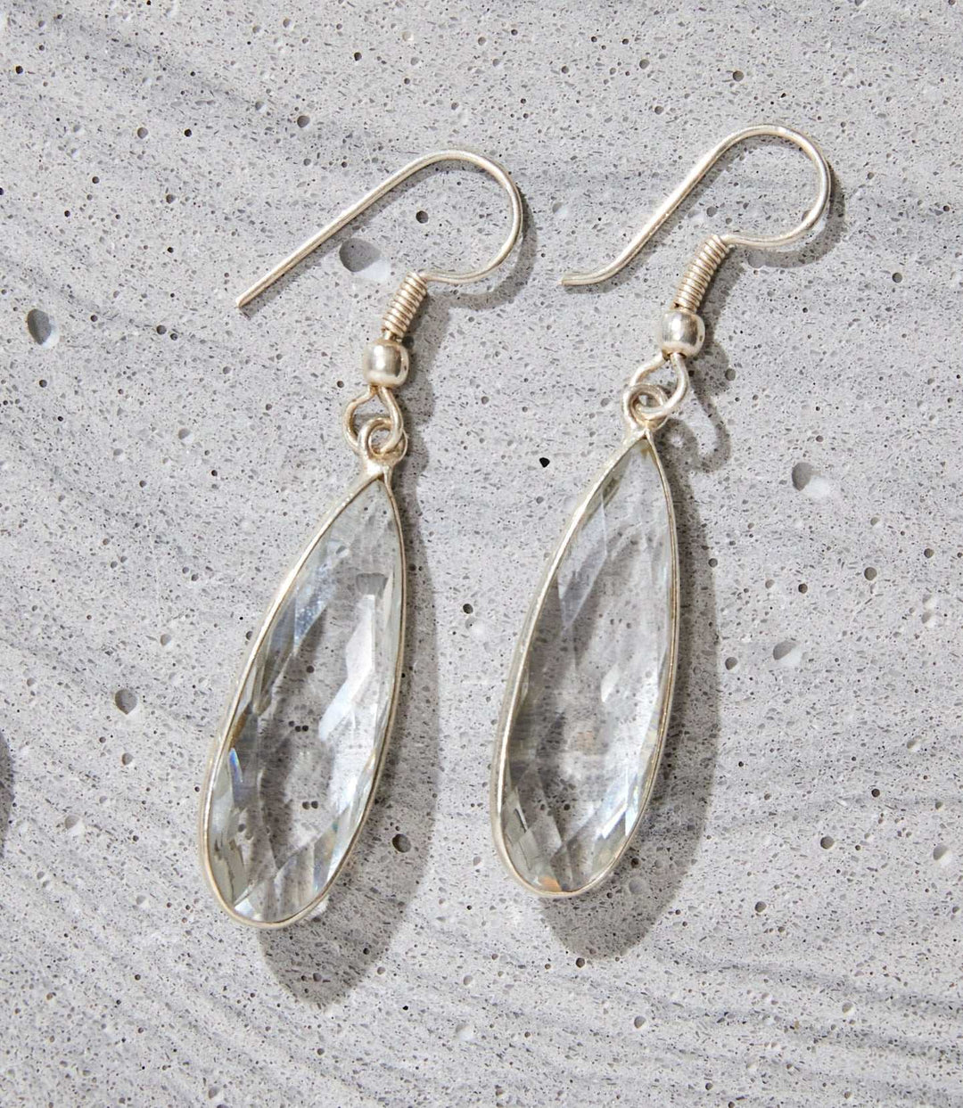 Silver-plated quartz teardrop dangle earrings showcasing clear quartz stones on a textured gray surface